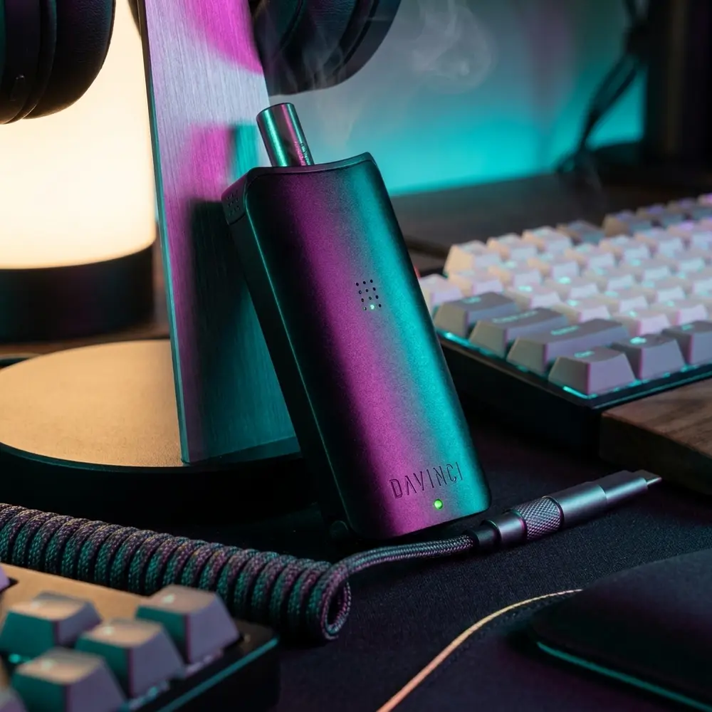 Bateria 510 Artiq DaVinci apoiada num setup gamer RGB, teclado e luzes coloridas ao fundo com vapor sutil - Vapor Gringo