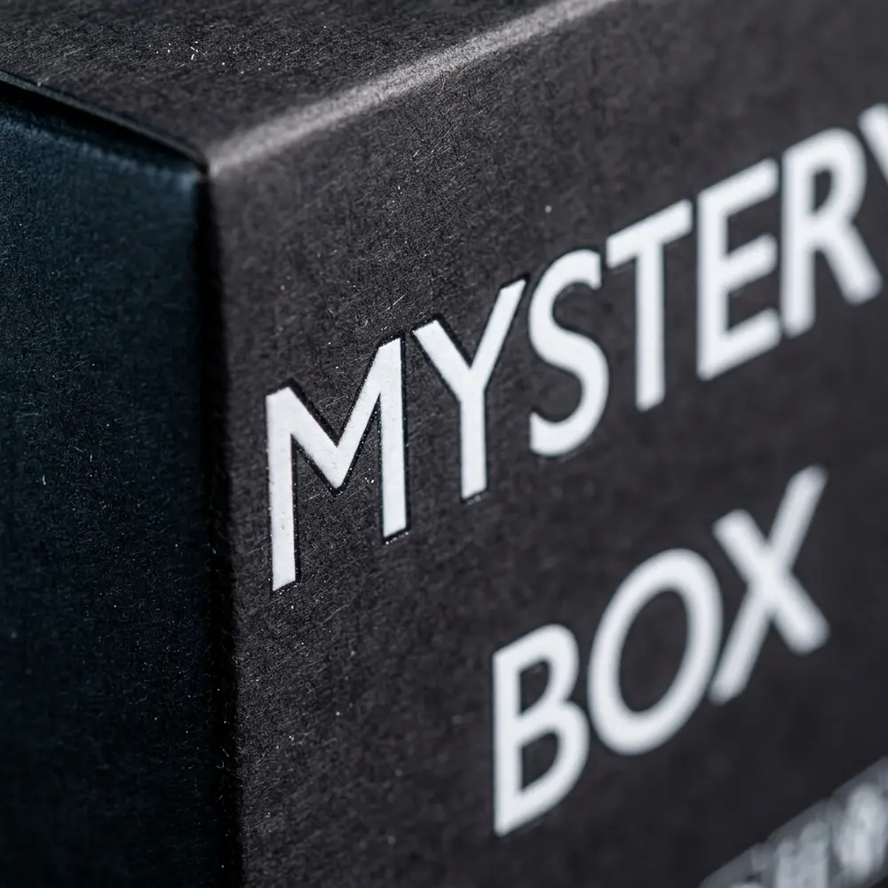 Detalhe da Black Box Vapor Gringo com logo, verniz localizado, relevo e textura do papel preto visíveis na borda - Vapor Gringo