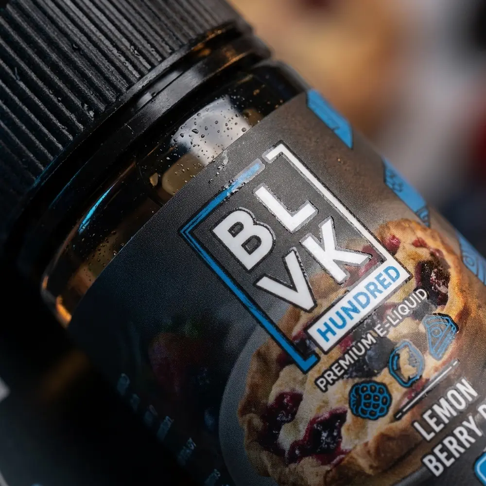 Detalhe do rotulo blvk unicorn lemon berry pie com gotas de condensacao, textura do vidro e brilho do nozzle - Vapor Gringo