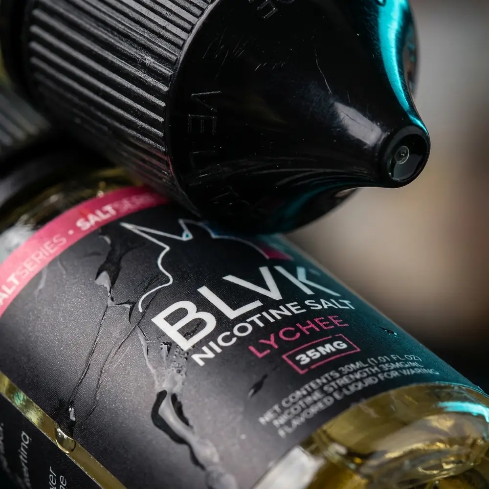 Close-up do rótulo e bico da garrafa BLVK Unicorn Lychee com gotas, texturas e reflexos finos - Vapor Gringo