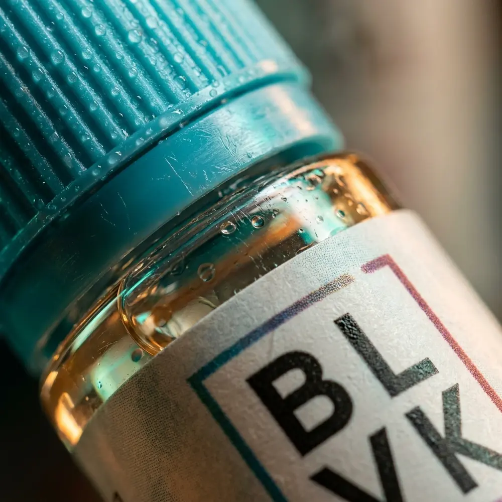 Macro do rotulo e bico da garrafa Blvk Unicorn Lychee Menthol com gotas de condensacao e micro-reflexos - Vapor Gringo