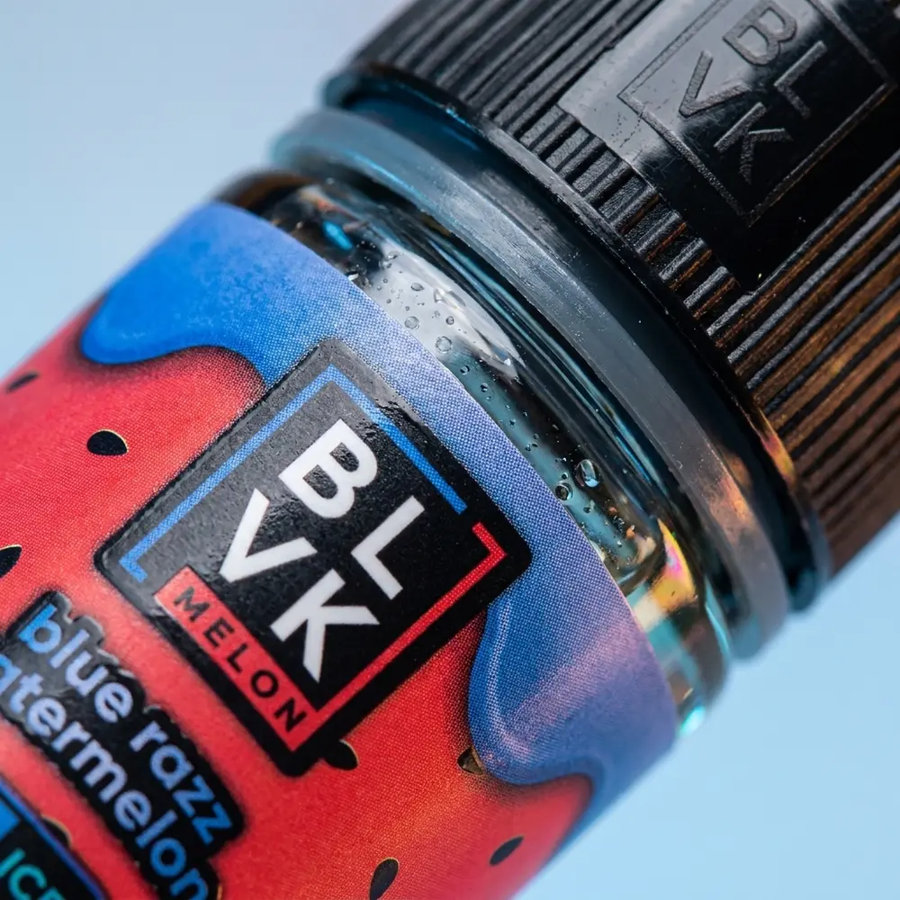 Detalhe do rótulo BLVK Unicorn Salt Blue Razz Watermelon Ice Melon mostrando texturas, gotículas e brilho metálico da tampa - Vapor Gringo