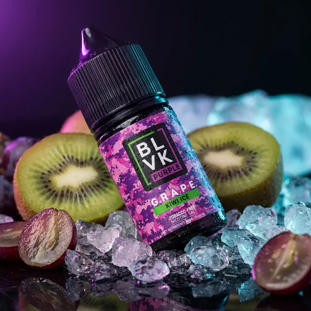 Frasco Blvk Unicorn Salt Grape Kiwi Ice sobre acrilico com gelo e frutas, iluminação roxa intensa. - Vapor Gringo