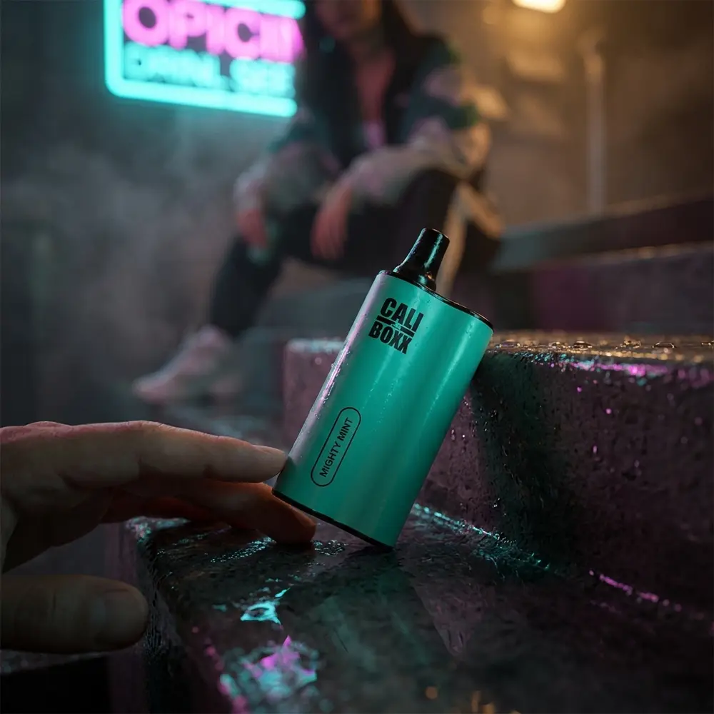Pod Cali Bars Boxx Mighty Mint apoiado em lancol molhado na rua com reflexos neon e mao aproximando-o - Vapor Gringo