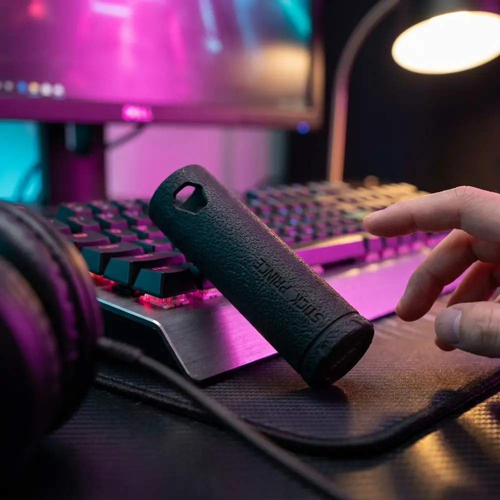 Capa de protecao Stick Prince apoiada em mesa gamer RGB, reflexos magenta e ciano, maos proximas - Vapor Gringo