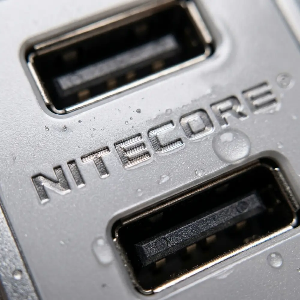 Close-up do logotipo e portas do carregador UA55 Nitecore com textura, reflexos e condensacao - Vapor Gringo