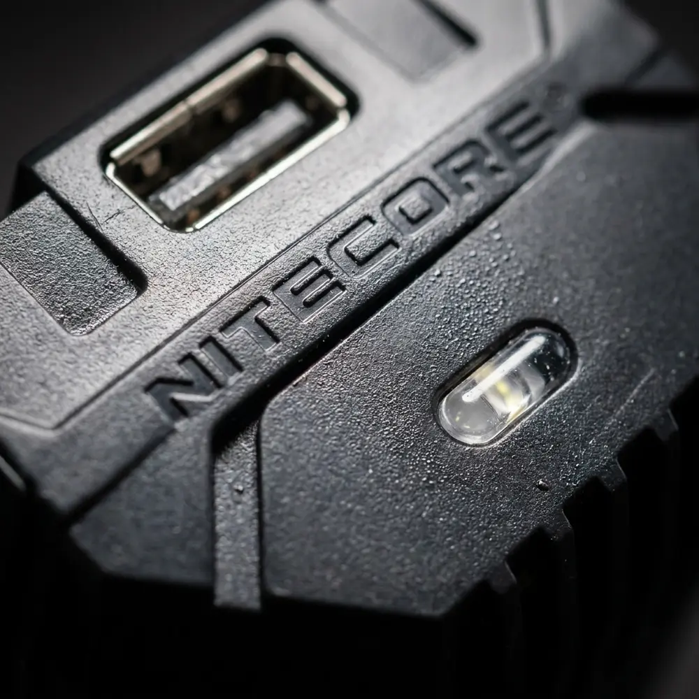 Macro do Carregador Veicular Nitecore V2 mostrando logo, textura do plastic e bordas metalicas com micro-reflexos - Vapor Gringo