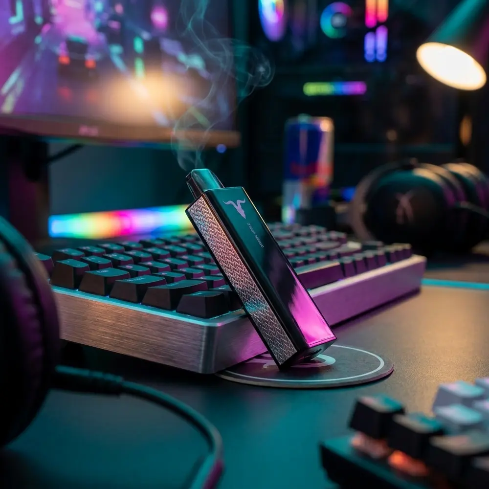 Cartucho refil Ignite P100 pousado no canto de uma mesa gamer RGB, reflexos coloridos e fundo desfocado - Vapor Gringo
