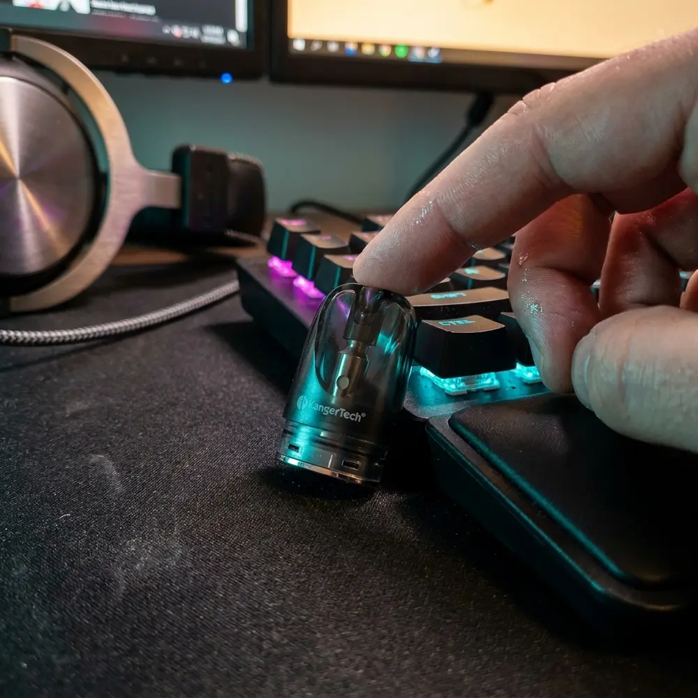 Cartucho UBOAT Kangertech em setup gamer RGB sobre mousepad, reflexos coloridos e dedo alcançando o pod para escala - Vapor Gringo
