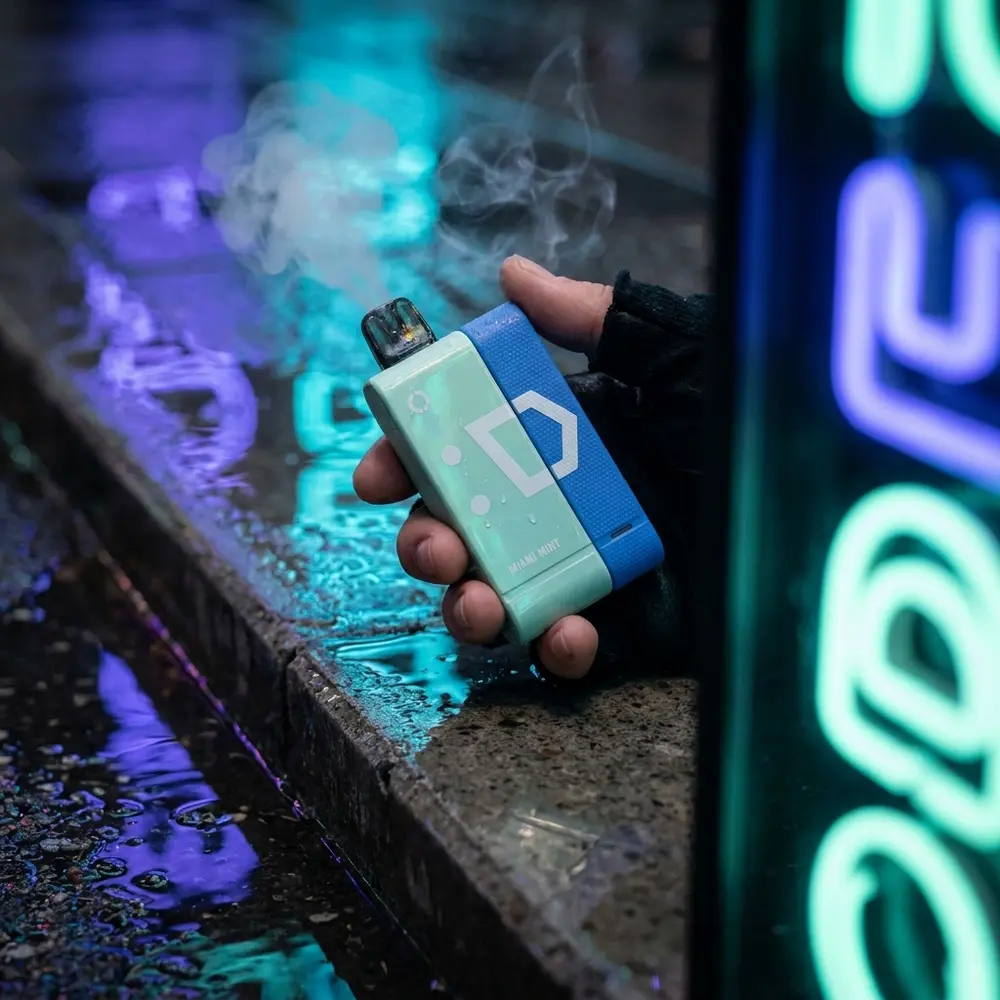 Pod Elf Bar EW9000 na mão à noite em rua urbana com letreiros neon azuis e reflexos verdes de menta - Vapor Gringo