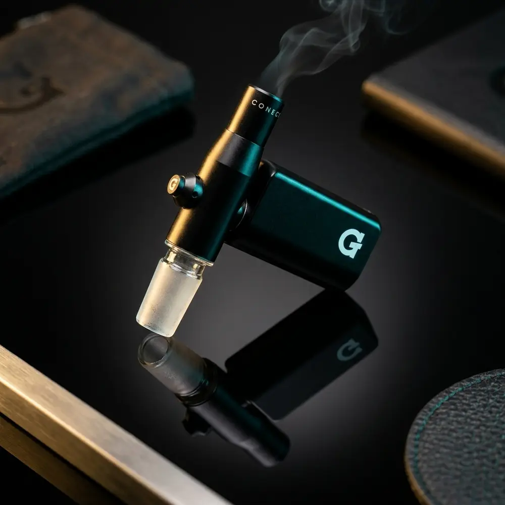 Vaporizador G Pen Connect suspenso sobre base acrílica preta com iluminação dourada e azul e reflexos metálicos - Vapor Gringo
