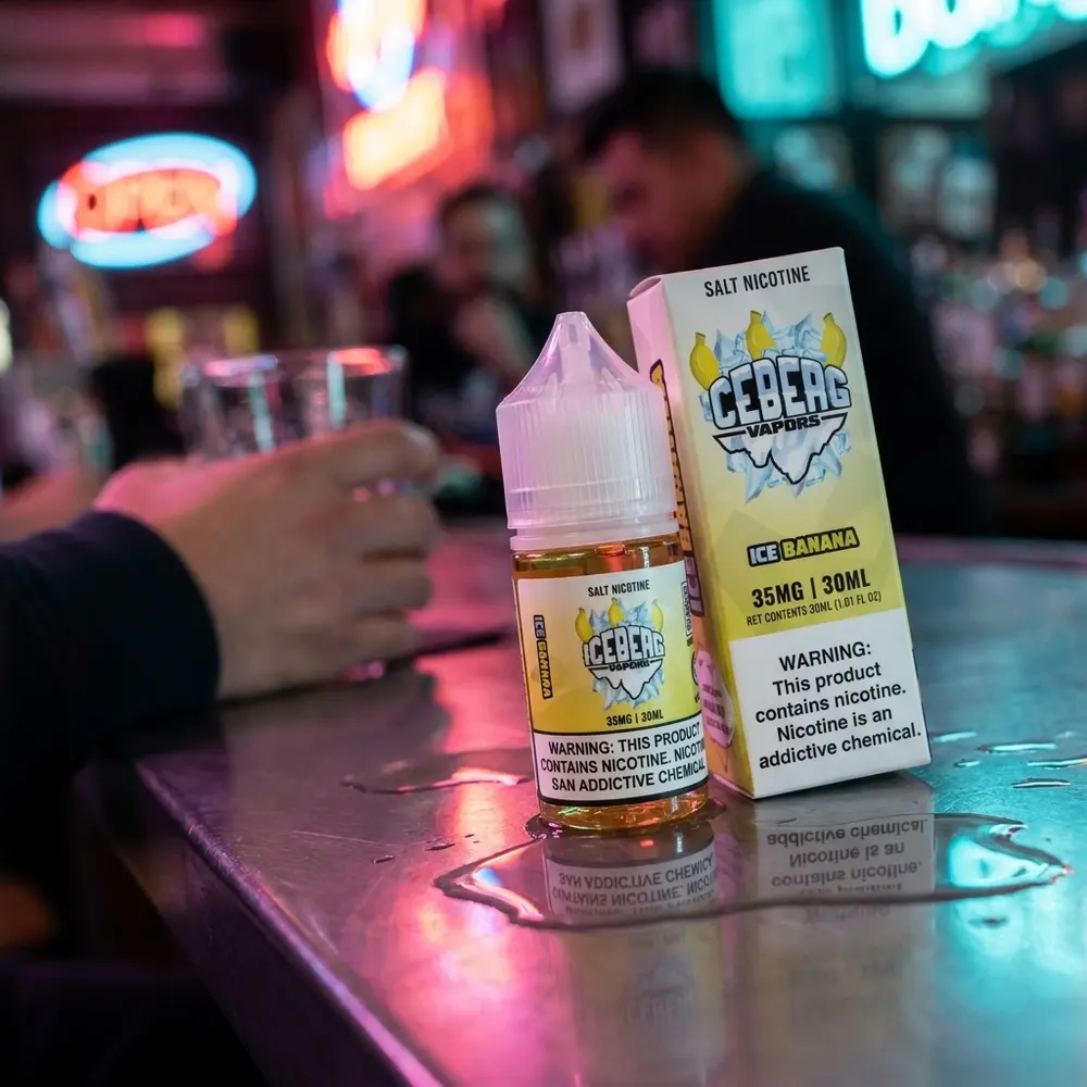 Frasco Iceberg Vapors Salt Ice Banana no balcão molhado de bar com bokeh neon urbano ao fundo - Vapor Gringo
