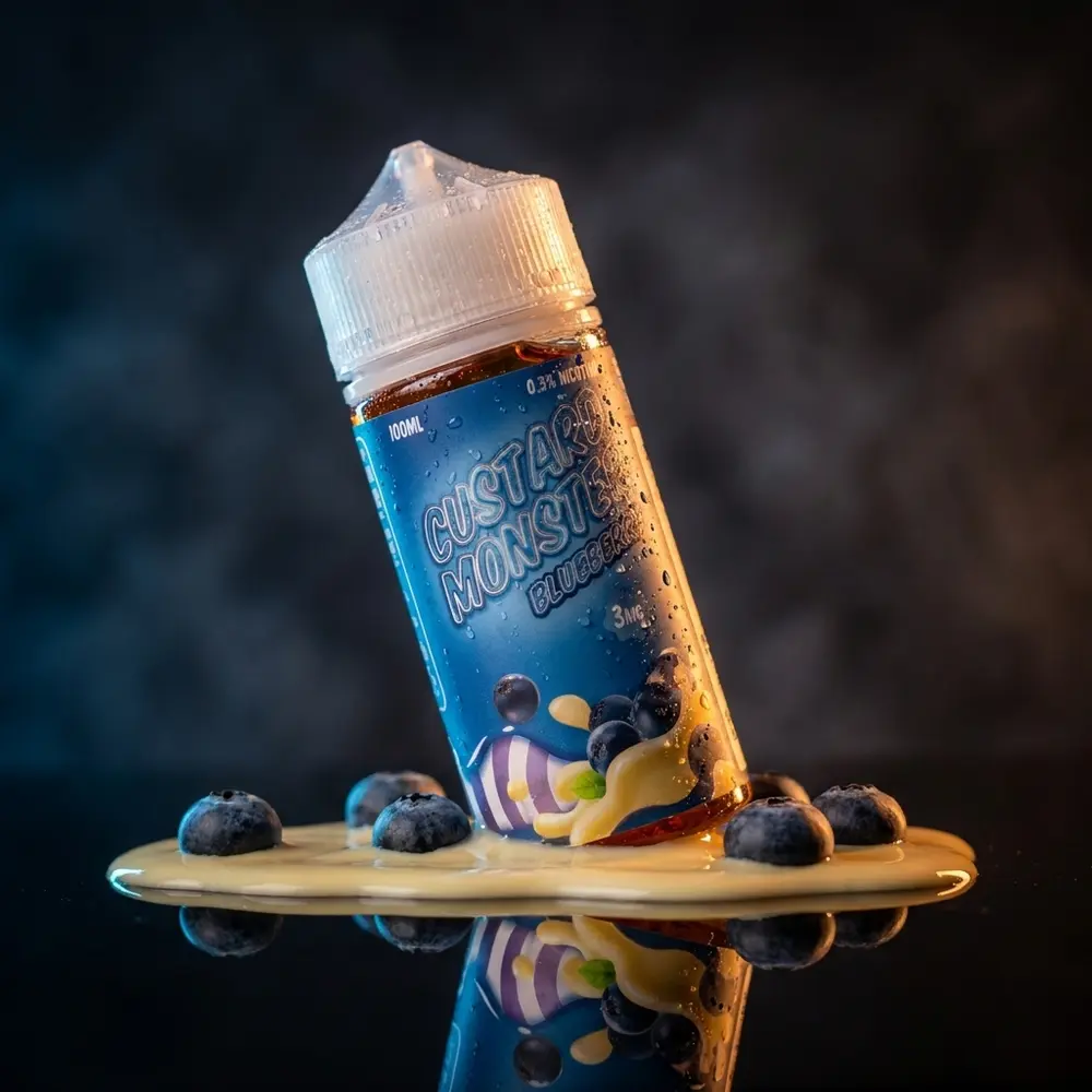 Garrafa do Líquido Jam Monster Blueberry Custard sobre acrílico preto com luzes azul e âmbar e reflexos cremosos. - Vapor Gringo