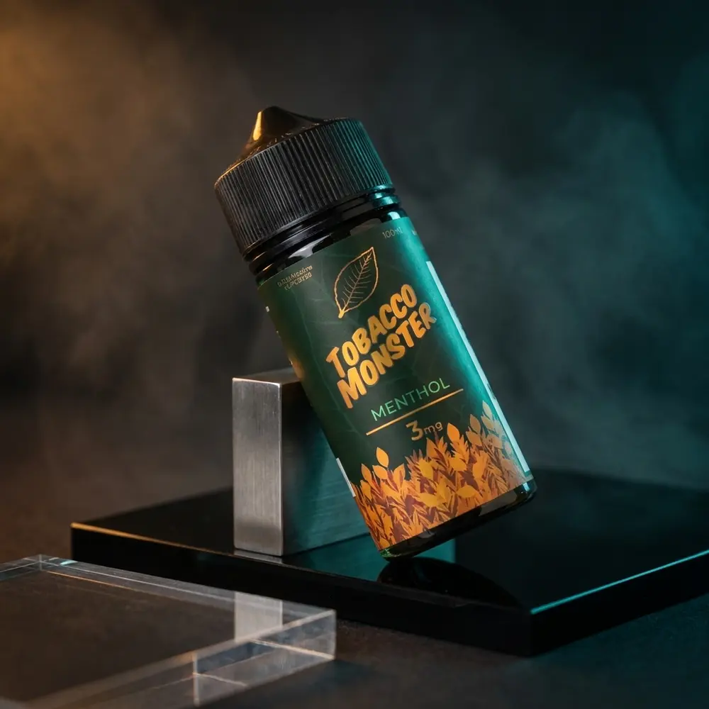 Frasco Jam Monster Tobacco Menthol sobre acrílico preto refletivo em estúdio premium, iluminação âmbar e azul - Vapor Gringo