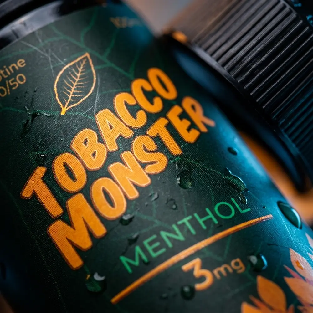 Macro do rótulo e bico da garrafa Jam Monster Tobacco Menthol com gotículas de condensação e reflexos - Vapor Gringo