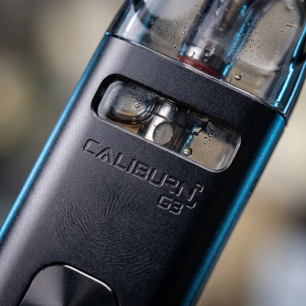 Close-up do Caliburn G3 mostrando logo, acabamento metalizado, janela do pod e gotas de condensacao - Vapor Gringo