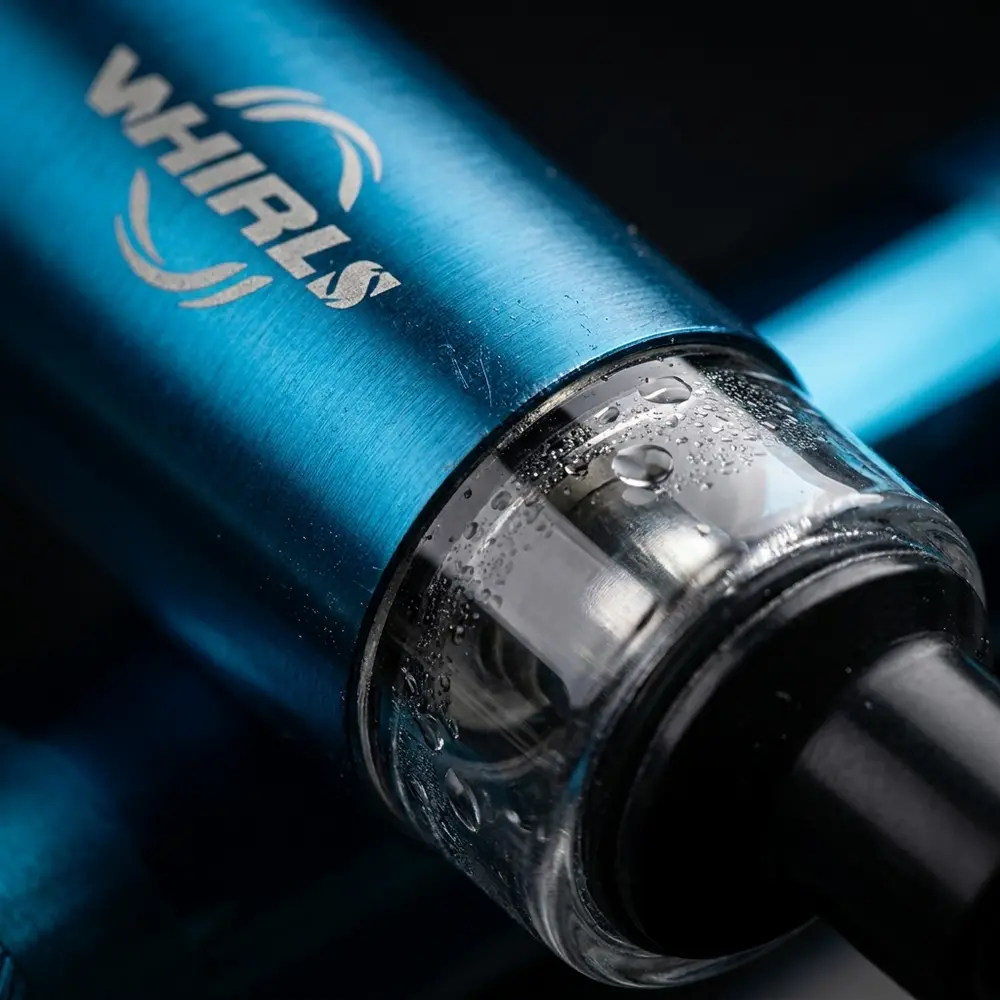 Detalhe macro do Kit Pod Mod Whirl S da Uwell mostrando logo, metal escovado, vidro do tanque e gotas de condensacao - Vapor Gringo