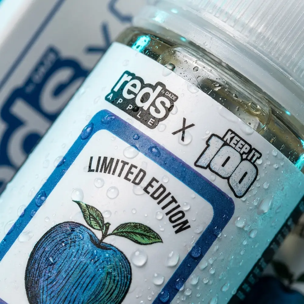 Close-up do rótulo do Líquido 7 Daze Reds Apple x Keep It 100 - Slapple Menthol com gotas, textura do rótulo e reflexos metálicos - Vapor Gringo