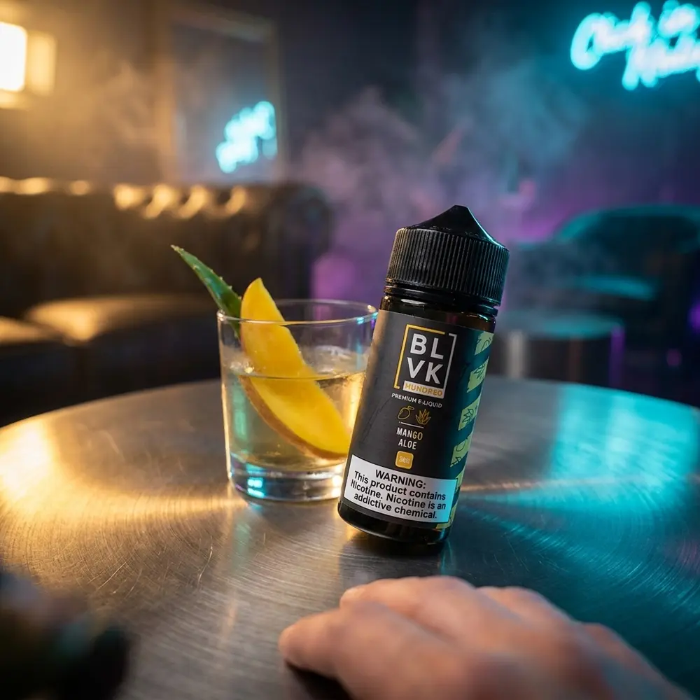 Garrafa Blvk Unicorn Mango Aloe 100ml em mesa de lounge luxuosa com copo de manga e luzes noturnas ao fundo. - Vapor Gringo