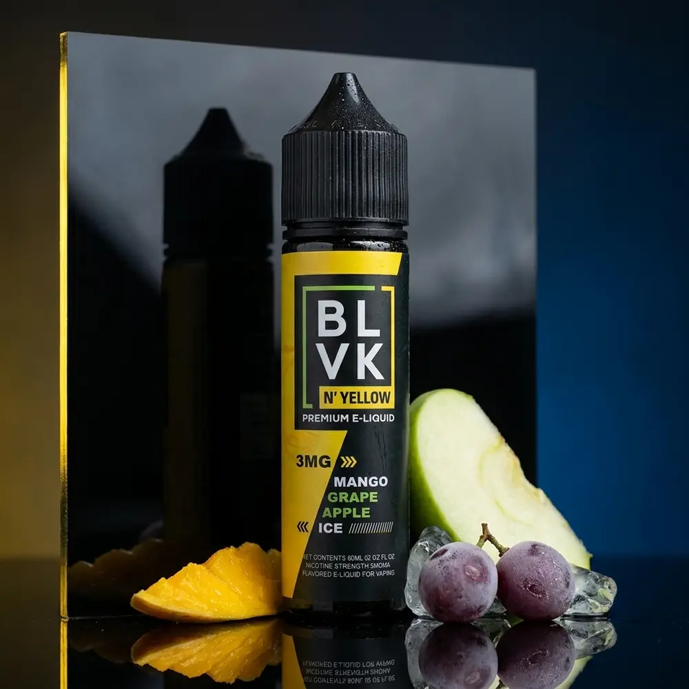 Frasco de líquido Blvk Unicorn Yellow (Mango Grape Apple Ice) sobre acrílico preto, frutas e luzes amarelas e azuis - Vapor Gringo