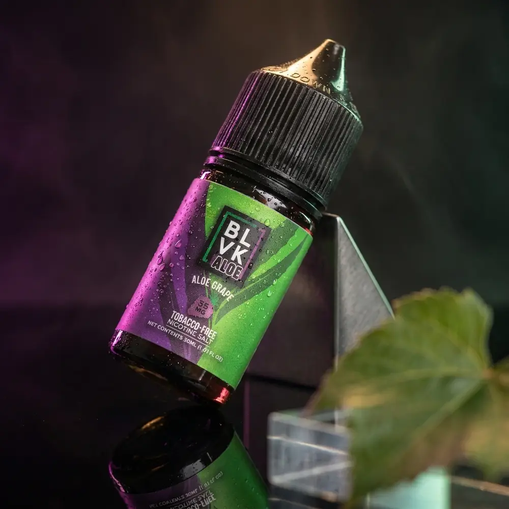 Garrafa Liquido Blvk Unicorn Salt Aloe Grape sobre acrilico preto com gotas e luzes roxas e verdes ao fundo - Vapor Gringo