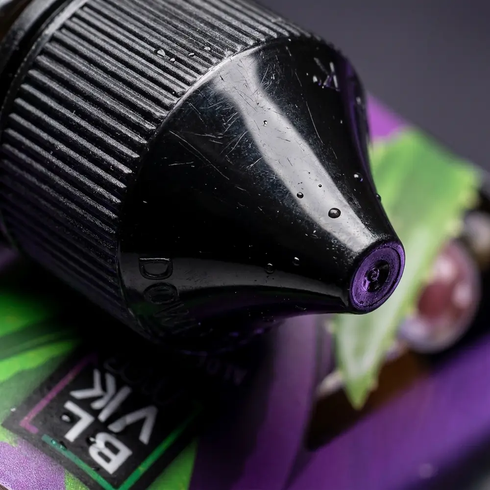 Macro do rótulo e bocal da garrafa Liquido Blvk Unicorn Salt Aloe Grape com gotas, reflexos e textura do rótulo - Vapor Gringo