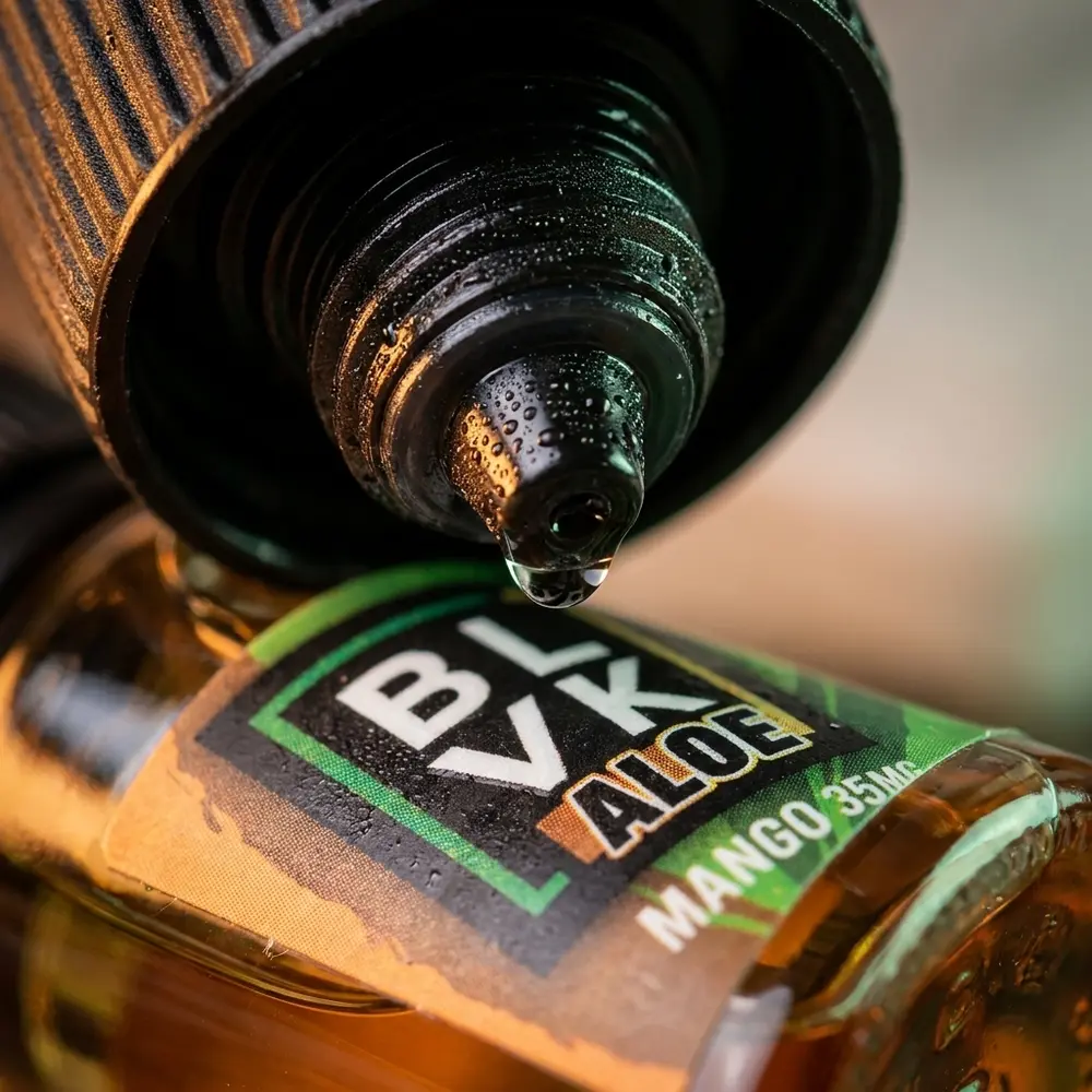 Macro do rótulo e bico da garrafa Blvk Unicorn Salt Aloe Mango com gota de líquido e condensação - Vapor Gringo