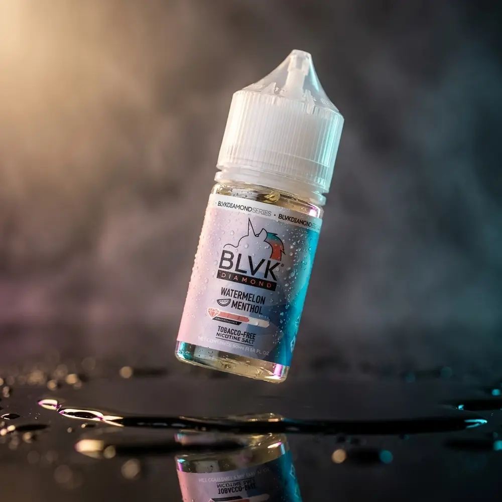 Frasco de Líquido Blvk Unicorn Salt Watermelon Menthol Diamond inclinado sobre acrílico preto molhado com reflexos coloridos - Vapor Gringo