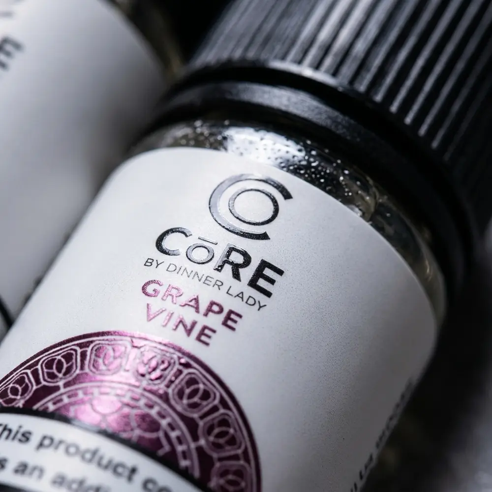 Detalhe do rótulo Líquido Core Dinner Lady Grape Vine com gotas, textura do vidro e reflexos do verniz - Vapor Gringo