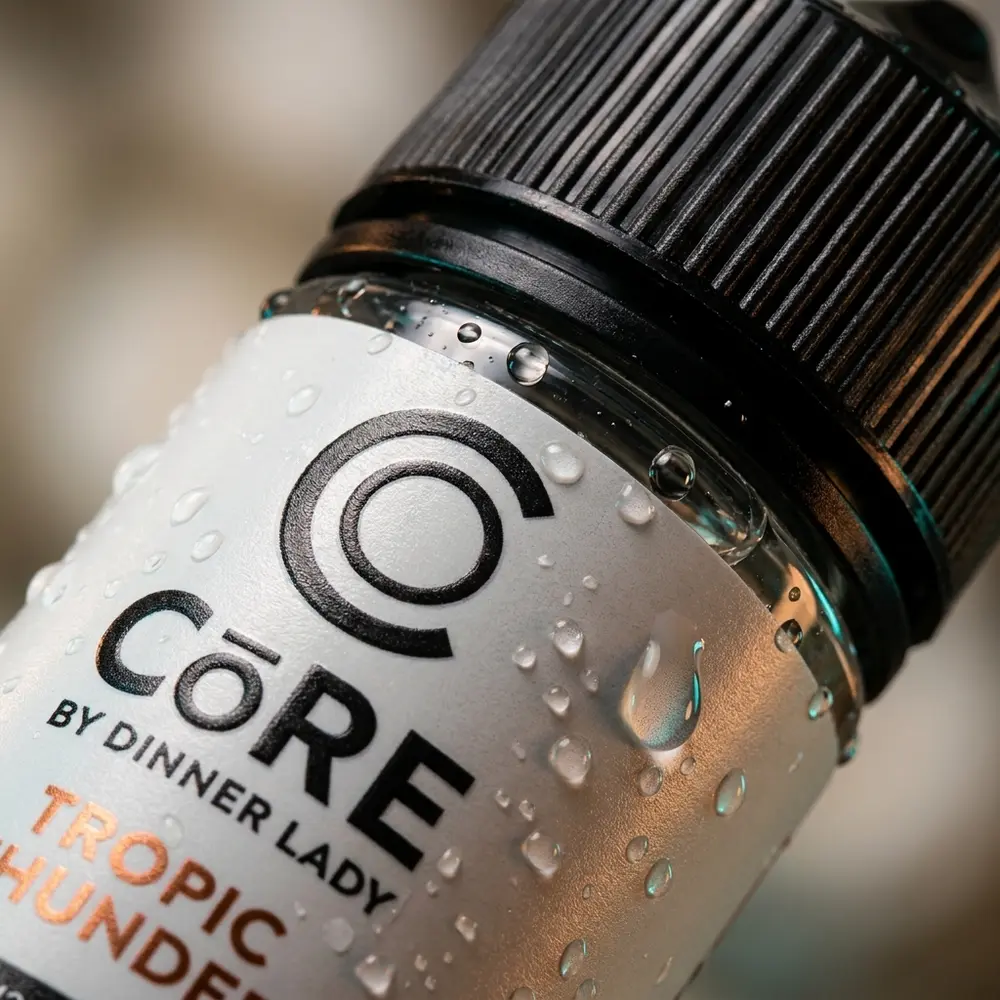 Detalhe macro do rótulo e do bico da garrafa Líquido Core Tropic Thunder 120ml com gotas de condensação - Vapor Gringo