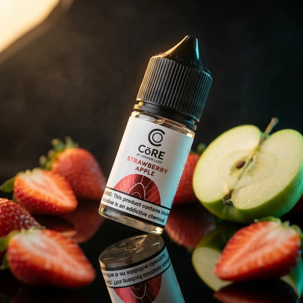 Frasco 30ml Líquido Core Strawberry Apple da Dinner Lady em close sobre base acrílica com morango e maçã próximos - Vapor Gringo