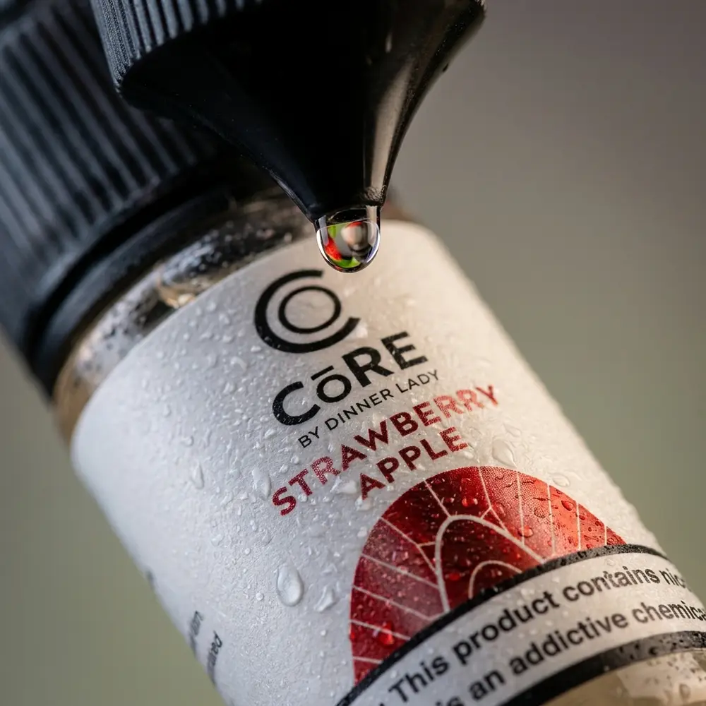 Macro do rótulo do Líquido Core Strawberry Apple mostrando textura do papel, gotículas e bico conta-gotas - Vapor Gringo