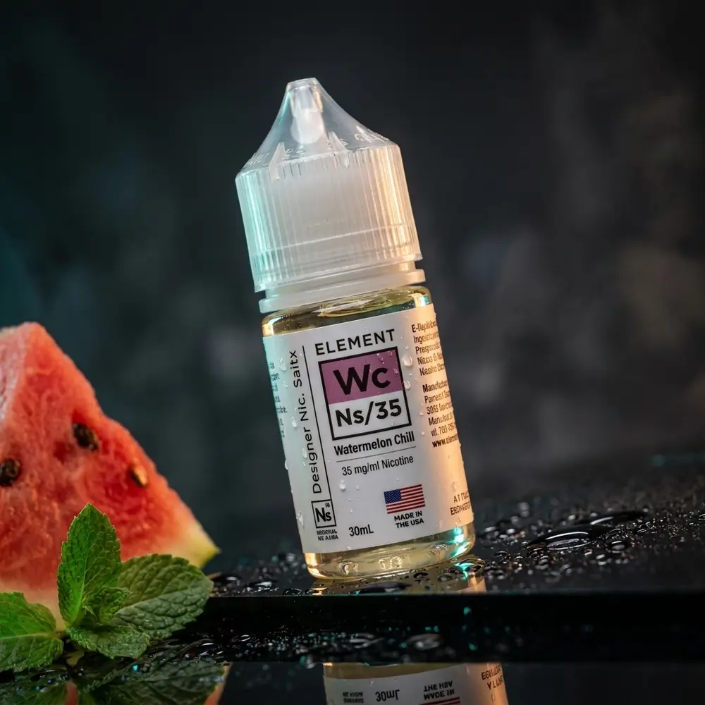 Garrafa do liquido Element Salt Watermelon Chill com condensacao sobre acrilico preto e fatia de melancia ao lado - Vapor Gringo