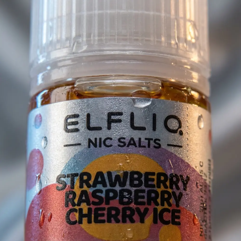 detalhe do rotulo e bocal do liquido Elf Liq Salt Strawberry Raspberry Cherry Ice com condensacao, textura do papel e reflexos - Vapor Gringo