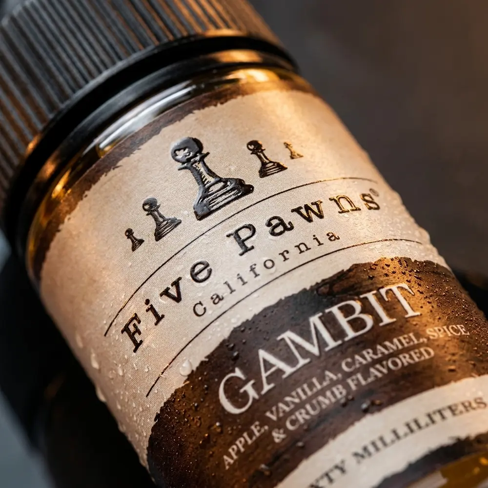 Close-up do rótulo e bico da garrafa Five Pawns Gambit 60ml com gotas, textura de vidro e reflexos de caramelo. - Vapor Gringo