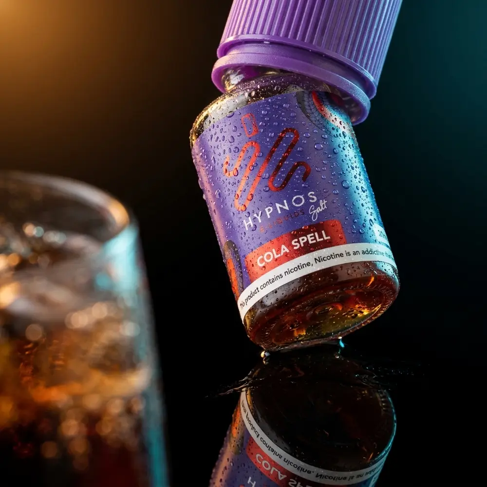 Frasco Hypnos Salt Cola Spell 30ml inclinado sobre acrílico preto com condensação e reflexo - Vapor Gringo