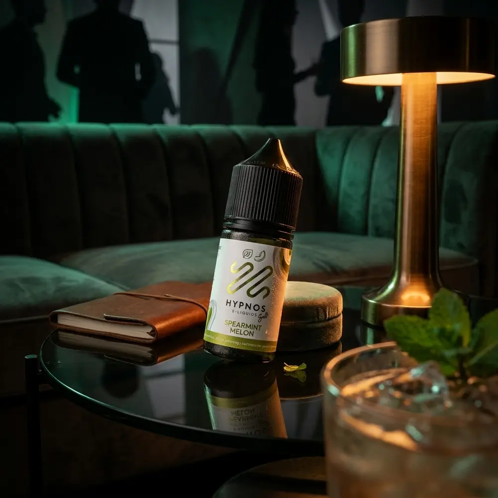 Garrafa do liquido Hypnos Salt Spearmint Melon sobre mesa de lounge com iluminacao ambiente e elementos de noite - Vapor Gringo