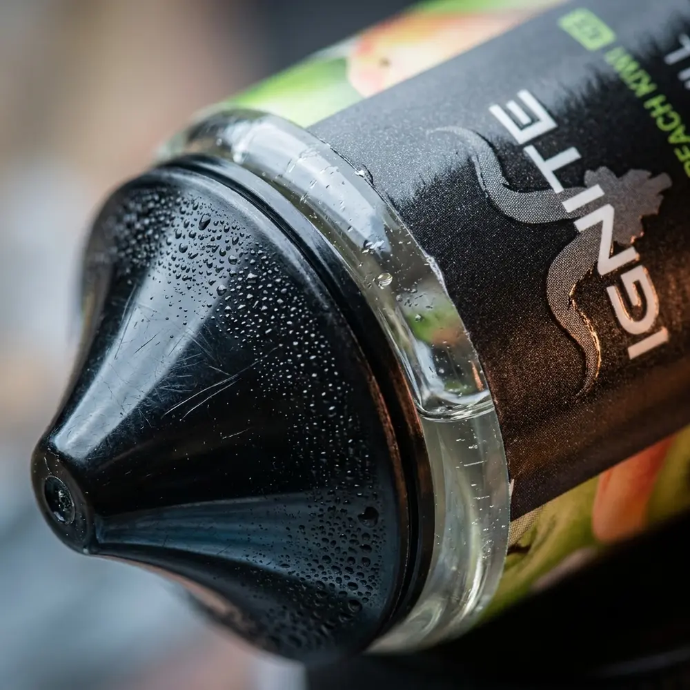 Detalhe macro do rótulo e bocal do Líquido Ignite Green Apple Peach Kiwi Ice com gotículas e reflexos metálicos - Vapor Gringo