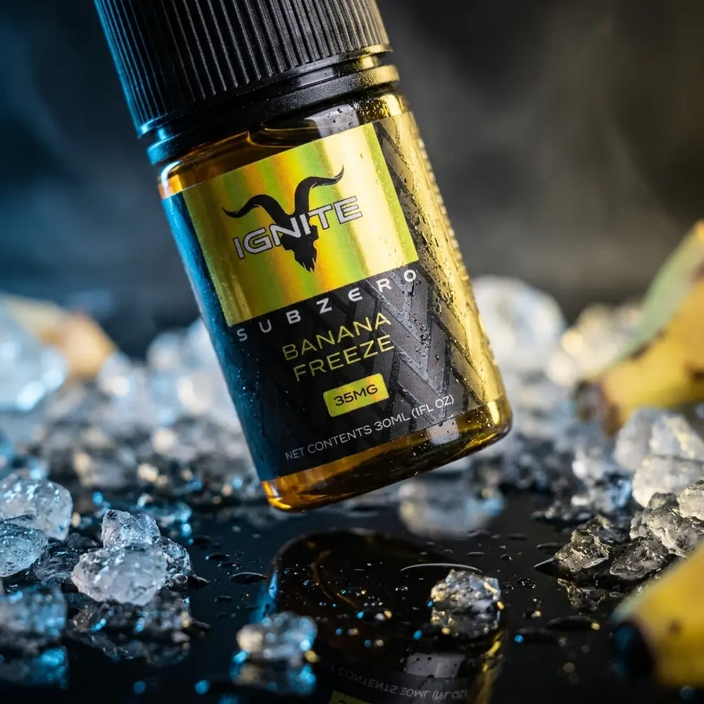 Garrafa do Liquido Ignite Salt SubZero Banana Freeze inclinada sobre acrilico com gelo e luzes frias e amarelas - Vapor Gringo
