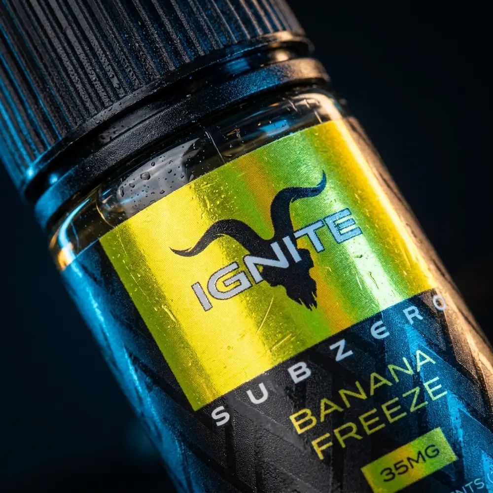 Close-up do rótulo e bico do Liquido Ignite Salt SubZero Banana Freeze com condensacao e reflexos metalicos - Vapor Gringo