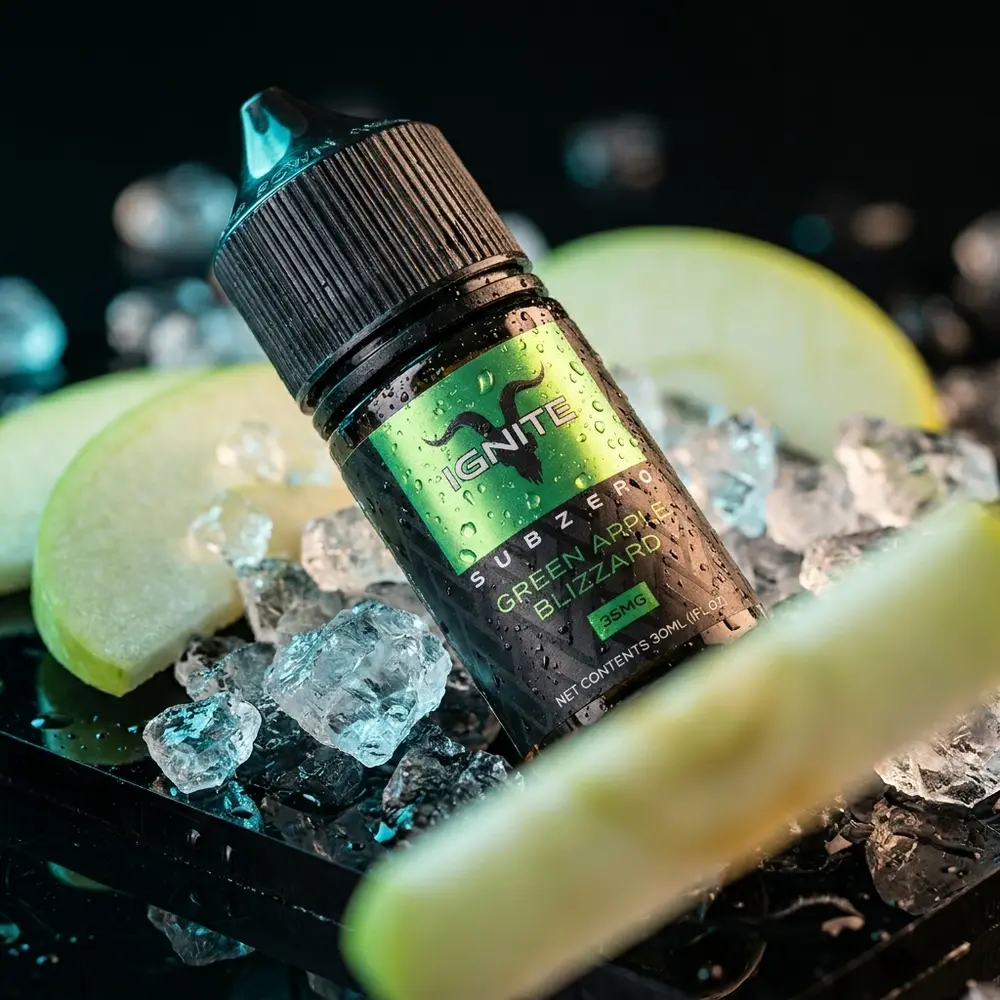 Frasco Líquido Ignite Salt SubZero Green Apple Blizzard sobre acrílico preto com gelo e fatias de maçã verde. - Vapor Gringo