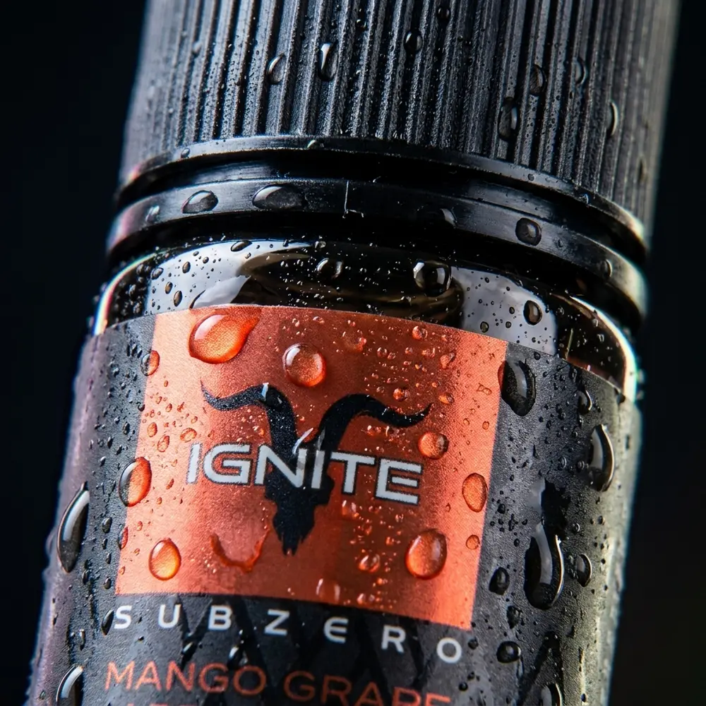 Detalhe macro do bocal, rótulo e gotículas da garrafa Líquido Ignite Salt SubZero Mango Grape Apple Pops. - Vapor Gringo