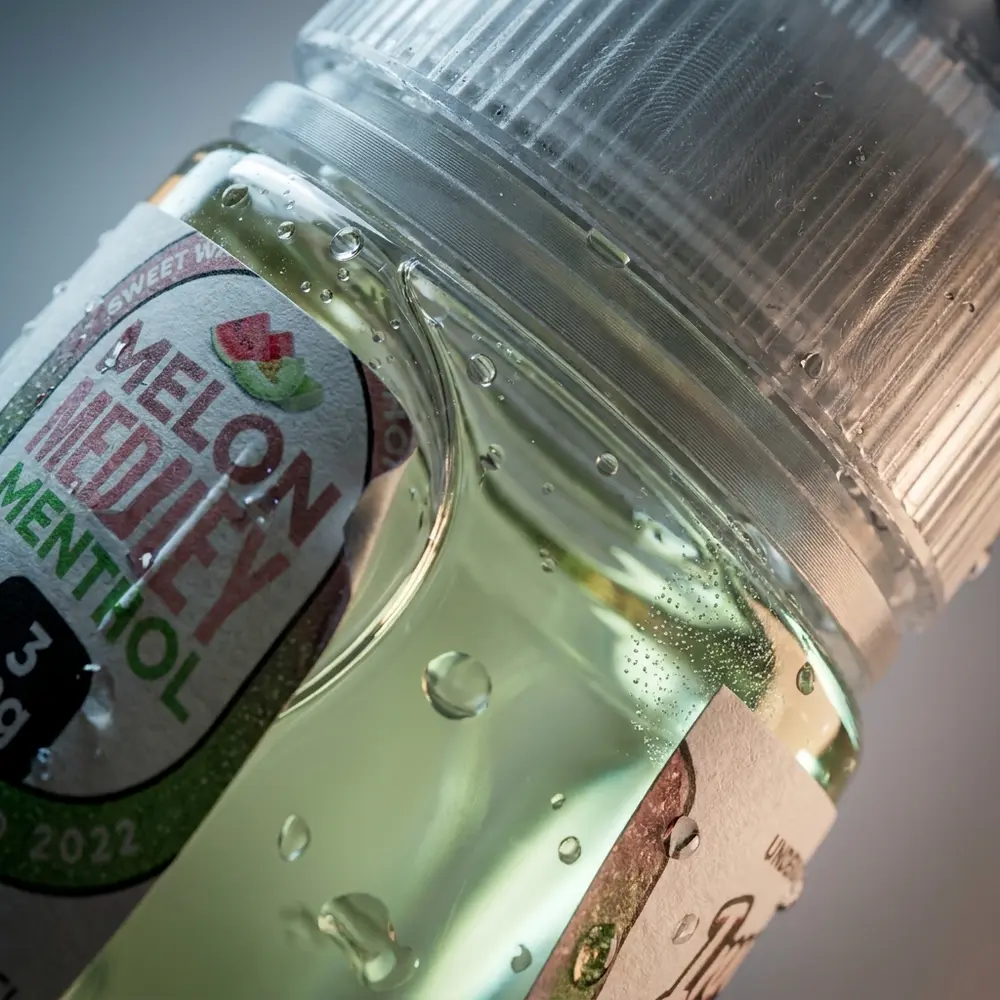 Close-up do rótulo e bico do frasco Liquido Innevape Melon Medley Menthol com condensação e reflexos - Vapor Gringo