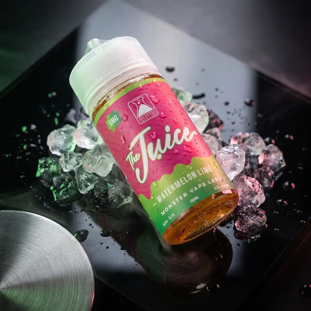 Frasco do Liquido Jam Monster Watermelon Lime sobre base acrilica refletiva, vapor sutil e elementos metalicos ao redor - Vapor Gringo