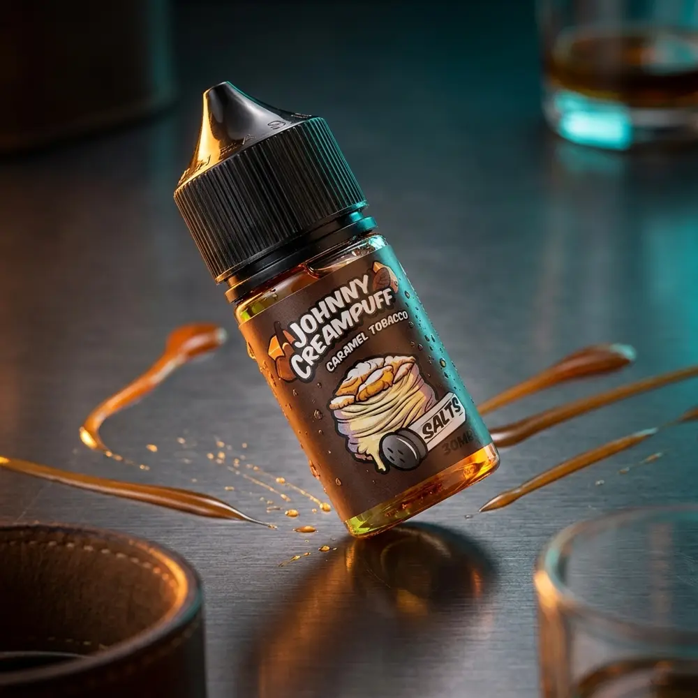 Garrafa Johnny Creampuff Salt Caramel Tobacco inclinada sobre superficie brilhante com caramelo e folhas de tabaco ao fundo - Vapor Gringo