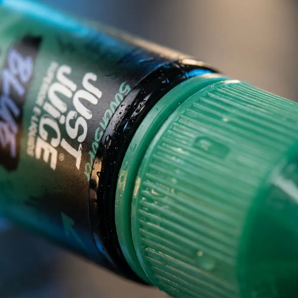 Close-up do rótulo e bico da embalagem Just Juice Salt Blue Mint com gotas de condensação e textura do rótulo - Vapor Gringo