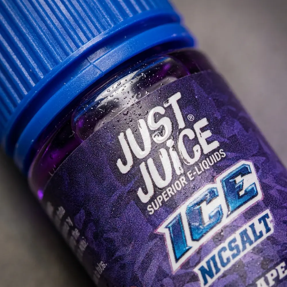Macro do frasco Just Juice Salt Grape Ice, foco no rótulo texturizado, gotículas e reflexos no bico - Vapor Gringo