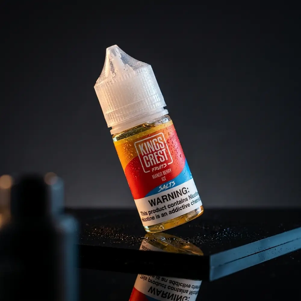 Garrafa Líquido Kings Crest Salt Mango Berry Ice suspensa sobre base acrílica escura com gotas e reflexos - Vapor Gringo