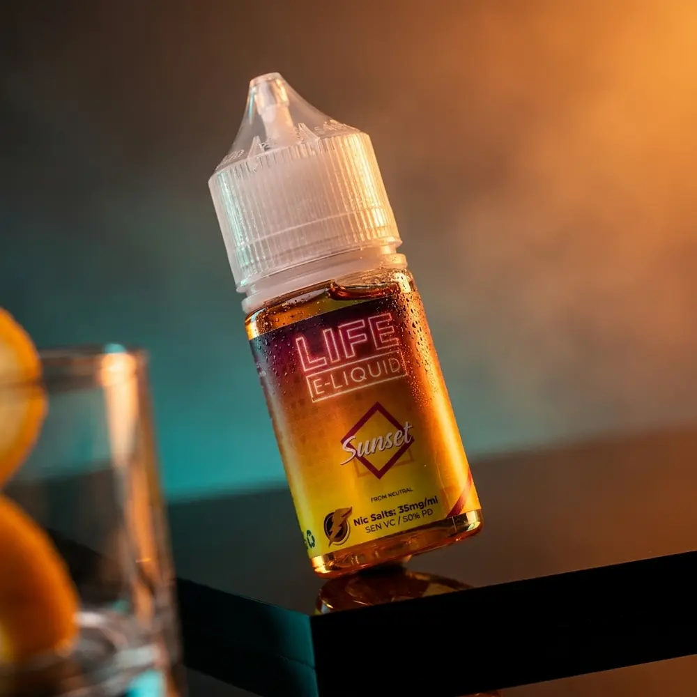Frasco do Liquido Life e-Liquid Salt - Sunset sobre base acrilica escura, reflexos quentes e azulados e condensacao - Vapor Gringo