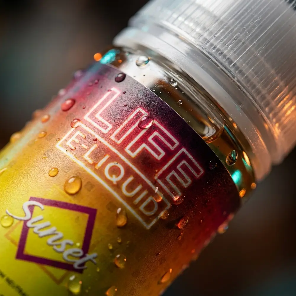 Detalhe macro do rótulo do Life e-Liquid Salt - Sunset com gotas de condensacao, textura do rótulo e bico visíveis - Vapor Gringo